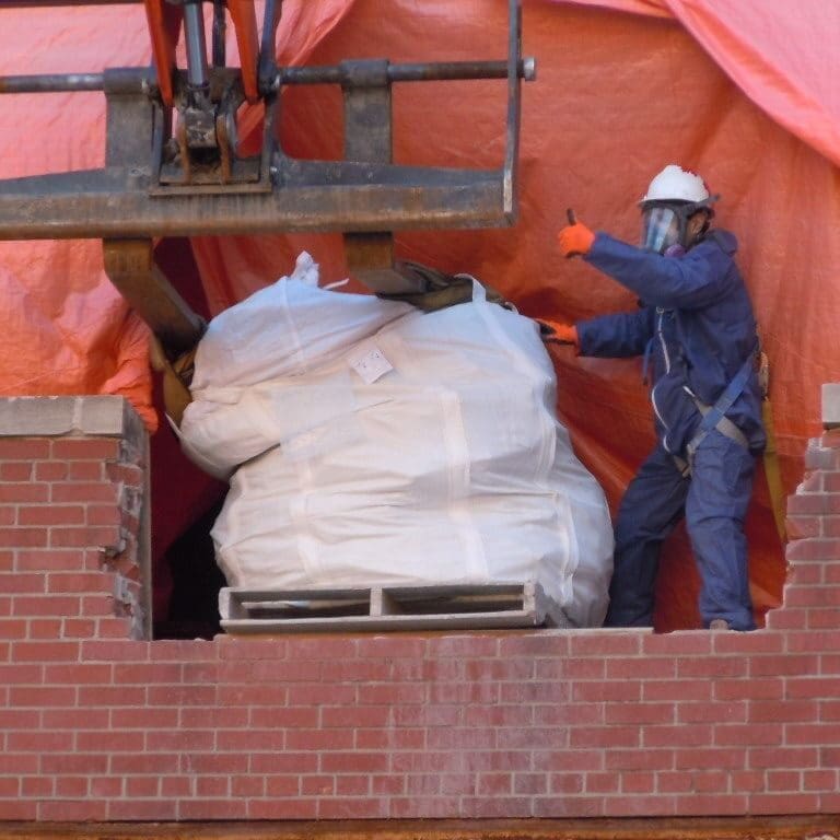 A person working with a machine operator to load up a bag of hazardous waste